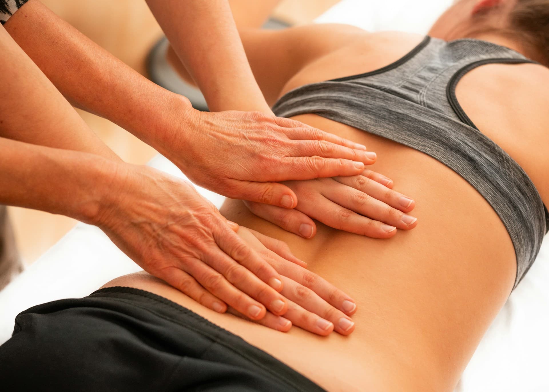 Two massage therapists performing a synchronized four-hand massage on a relaxed client, showing the rhythm and balance of this unique bodywork.